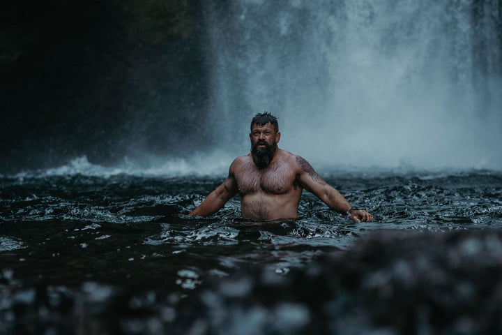 Man in cold wild river practicing cold water immersion for recovery